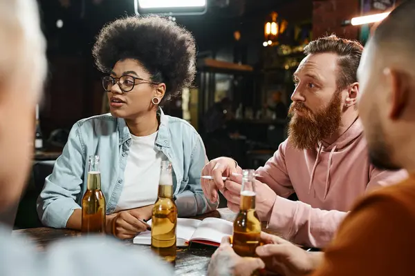 Amigos de trabalho multiétnicos atentos sentados perto de garrafas de cerveja no pub durante discussão de novo projeto — Fotografia de Stock