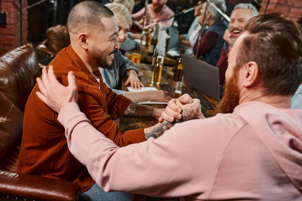 Happy multicultural workmates shaking hands near colleagues while spending time in pub after work — Stock Photo