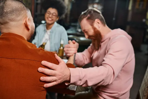 Blurred african american woman smiling near men shaking hands while sitting in pub after work — Stock Photo