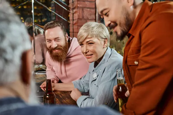 Sonrientes compañeros de trabajo multiculturales que escuchan a un colega borroso mientras planean un nuevo proyecto en el pub - foto de stock