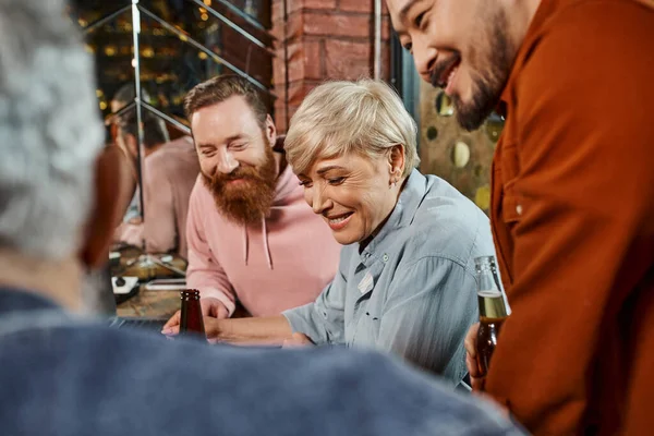 Gioiosi colleghi multietnici sorridenti vicino collega offuscata durante la discussione sulla nuova startup in pub — Foto stock