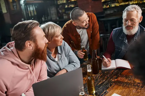 Equipe multiétnica ouvindo sorrir colega barbudo durante discussão do projeto de startup no pub — Fotografia de Stock