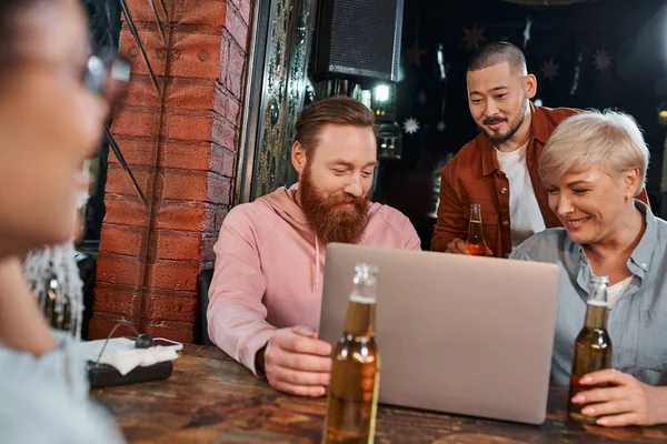 Sorrindo colegas multiétnicos olhando para laptop ao planejar novo projeto durante reunião no pub — Fotografia de Stock