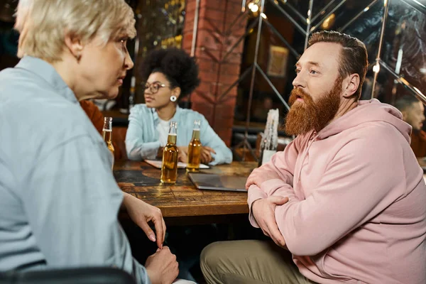 Homem barbudo e mulher de meia-idade falando perto de colega afro-americano durante reunião no pub — Fotografia de Stock
