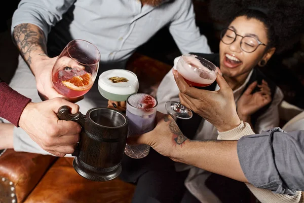 Схвильована афроамериканська жінка смердить коктейль окуляри з колегами в барі, корпоративна вечірка — стокове фото