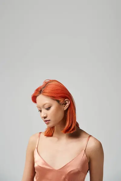 Young asian woman with dyed red hair posing in slip dress on grey background, fashion trend — Stock Photo
