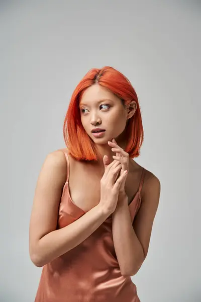 Portrait of dreamy young asian woman with red hair posing in silk slip dress on grey background — Stock Photo