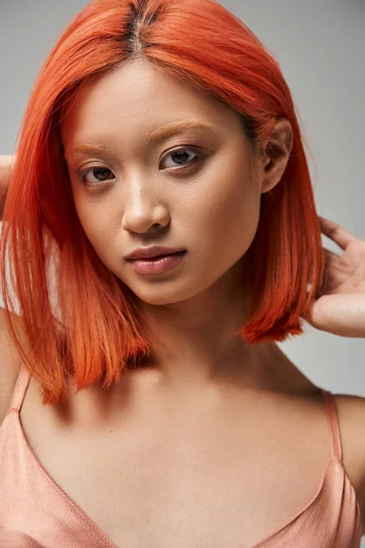 Porträt einer jungen Asiatin mit roten Haaren, die in die Kamera auf grauem Hintergrund blickt, natürliche Schönheit — Stockfoto