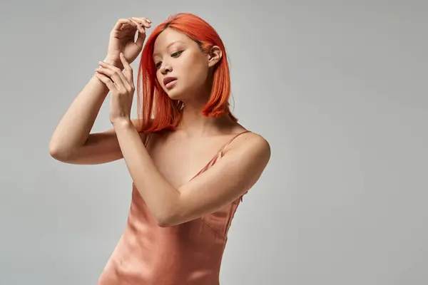 Портрет молодой азиатки с рыжими волосами, позирующей в скользящем платье на сером фоне, природная красота — стоковое фото