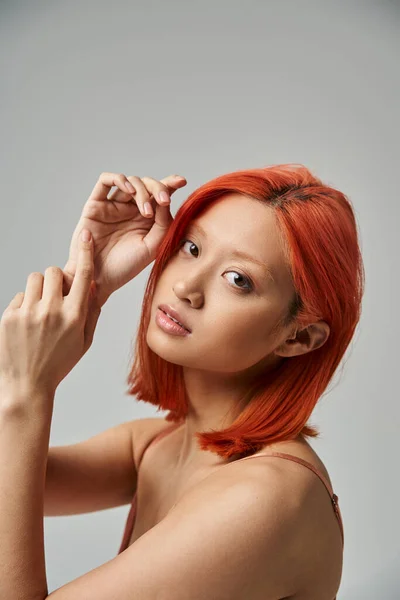 Porträt einer hübschen asiatischen Frau mit gefärbten Haaren, die in die Kamera auf grauem Hintergrund blickt, natürliche Schönheit — Stockfoto
