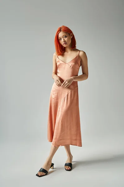 Sensual asian woman with red hair posing in silk slip dress on grey background, female elegance — Stock Photo