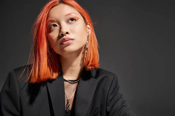 Portrait of pretty asian woman with red hair and piercing looking at camera on grey backdrop — Stock Photo