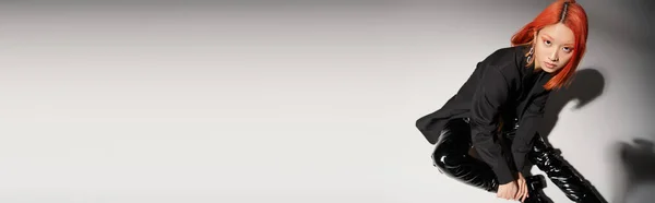 Hohe Winkel der asiatischen Frau in sexy Latexstiefeln und Blazer sitzt auf grauem Hintergrund, Banner — Stockfoto