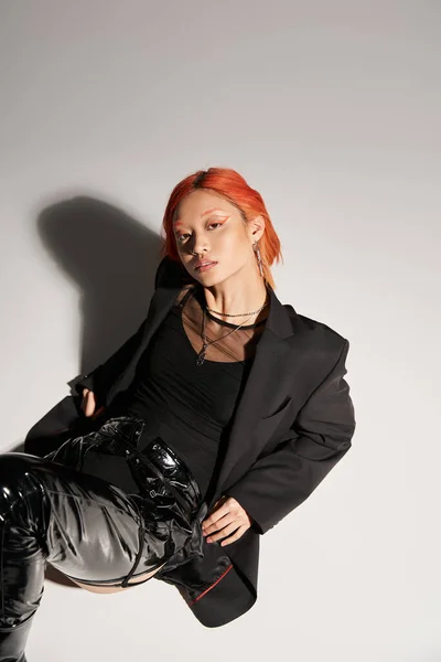 Top view of asian woman with red hair posing in bold outfit on grey background, black latex — Fotografia de Stock