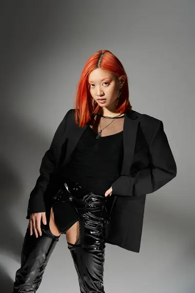 Asiatisches Model mit roten Haaren posiert mit der Hand an der Hüfte, in Latexstiefeln und übergroßem Blazer — Stockfoto