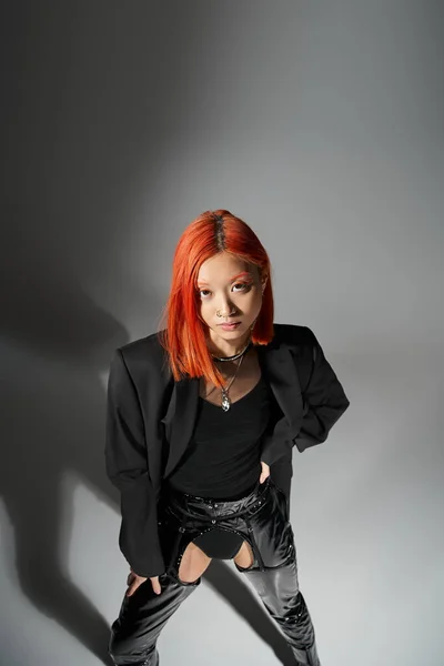 Stylish asian model with red hair and pose piercing posing with hand on hip, standing in blazer — Stock Photo