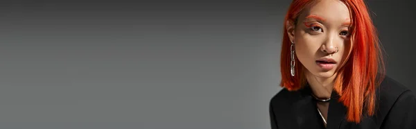 Portrait de modèle asiatique élégant avec des cheveux roux et pose piercing posant sur fond gris, bannière — Photo de stock