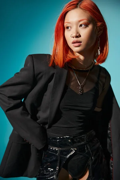 Elegante asiático modelo com vermelho cabelo e nariz piercing posando em oversized blazer no azul pano de fundo — Fotografia de Stock