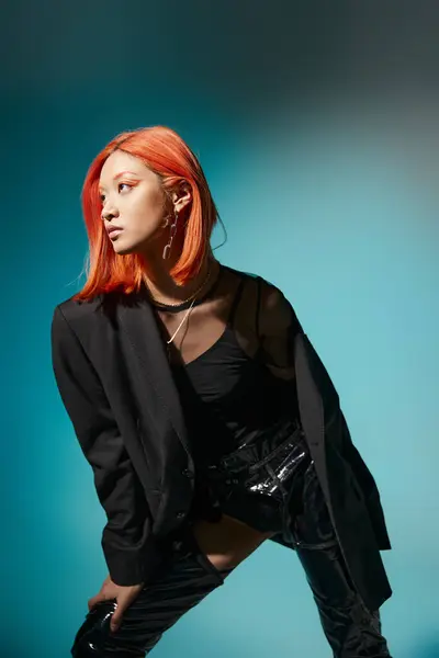 Modèle asiatique aux cheveux roux et piercing posant en blazer surdimensionné et latex noir sur fond bleu — Photo de stock