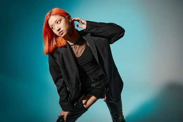Asiatisches Model mit roten Haaren und Piercing posiert in schwarzem Latex und übergroßem Blazer auf blauem Hintergrund — Stockfoto
