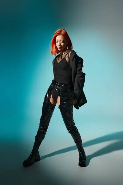 Full length of asian model posing in oversized blazer and black latex boots on blue backdrop — Stock Photo