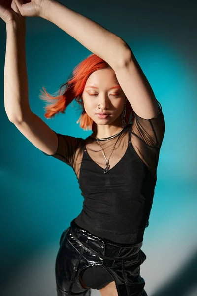Young asian model with closed eyes posing in transparent blouse and black latex on blue backdrop — Stock Photo