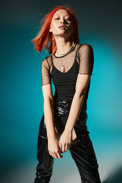 Pretty asian woman with piercing posing in black latex pants and transparent blouse on blue backdrop — Stock Photo