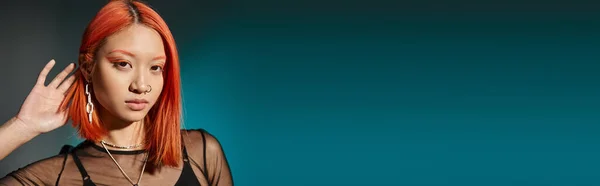 Porträt einer gepiercten Asiatin mit fettem Augen-Make-up und trendigem Ohrring auf blauem Hintergrund, Banner — Stockfoto