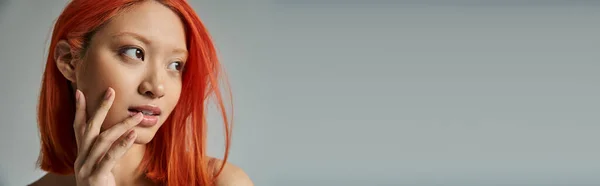 Belleza asiática, mujer joven con el pelo rojo y maquillaje natural mirando hacia otro lado y tocando mejilla, bandera - foto de stock