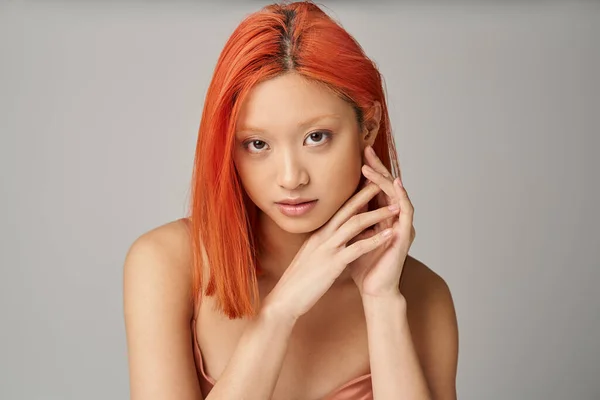 Retrato de encantadora joven mujer asiática con la piel perfecta mirando a la cámara sobre fondo gris - foto de stock
