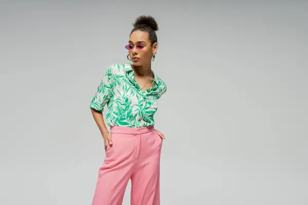 Stylish african american woman in pink sunglasses shirt with green pattern posing on grey backdrop — Stock Photo