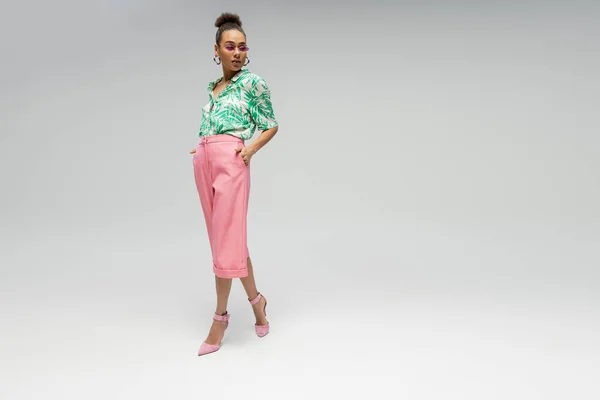Stylish african american woman in pink sunglasses and stylish attire posing on grey backdrop — Stock Photo
