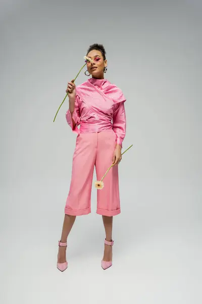 Полная длина довольно африканская американская женщина в розовом одеянии и солнцезащитные очки позируя с цветами — стоковое фото