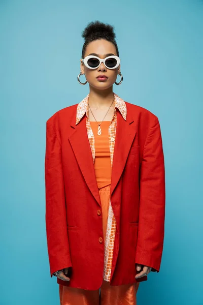 Mulher americana africana na moda em óculos de sol na moda e roupa vibrante posando em pano de fundo azul — Fotografia de Stock