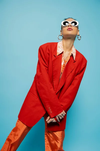 Donna afroamericana carismatica in occhiali da sole alla moda e abito audace in posa su sfondo blu — Foto stock