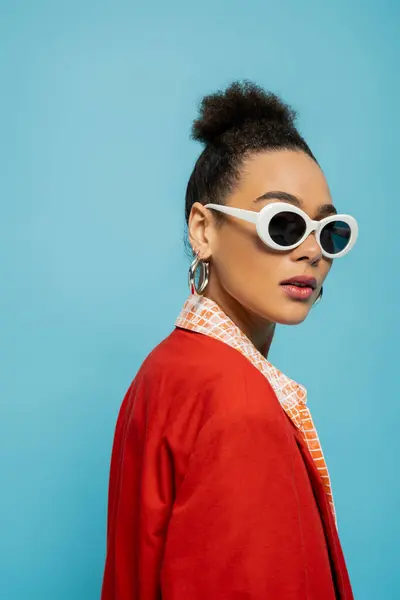 Accattivante modello africano americano in abito vivace e occhiali da sole su sfondo blu, ritratto — Foto stock