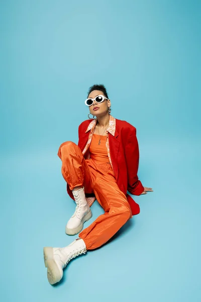 Fashion-forward, expressive african american model in trendy outfit sitting on blue background — Stock Photo