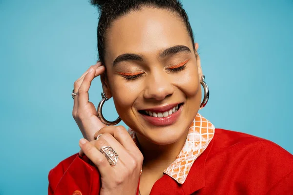 Portrait of pleased african american model in silver accessories smiling on blue backdrop — Stock Photo