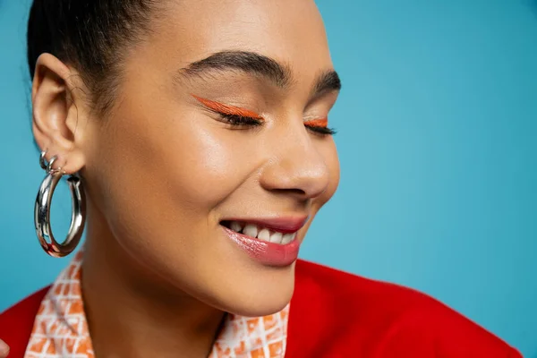 Close up of pleased african american model in silver accessories smiling on blue background — Stock Photo