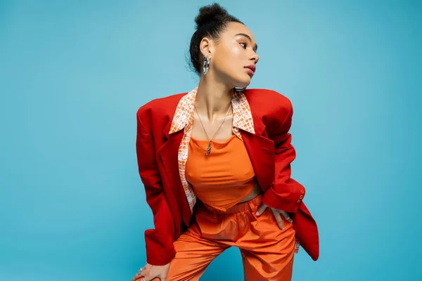 Elegante modelo afro-americano em negrito colorido traje e aro brincos posando no fundo azul — Stock Photo