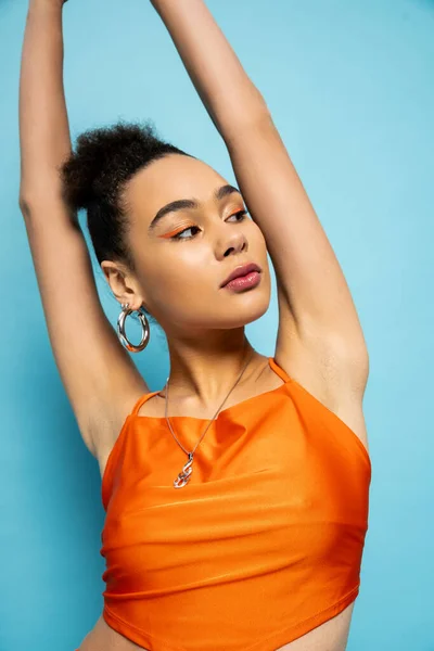Portrait of attractive young model with hoop earrings posing on blue background with her arms raised — Stock Photo