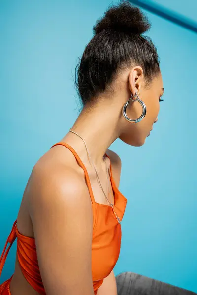 Trendy african american fashion model in striking orange outfit with hoop earrings looking away — Stock Photo
