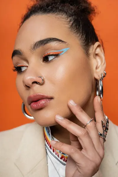 Retrato de mujer atractiva con maquillaje llamativo y accesorios mirando hacia otro lado, mano a cara - foto de stock