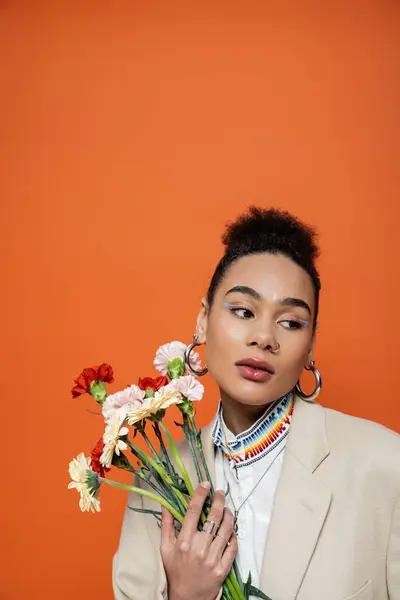 Elegante modelo de moda atractiva con maquillaje brillante y pendientes de aro posando con ramo de flores - foto de stock