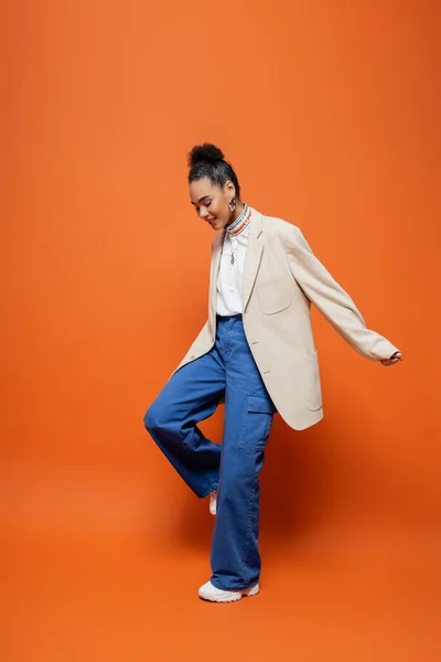 Modelo de moda americana africana alegre em blazer bege e calças azuis sorrindo olhando para baixo — Fotografia de Stock