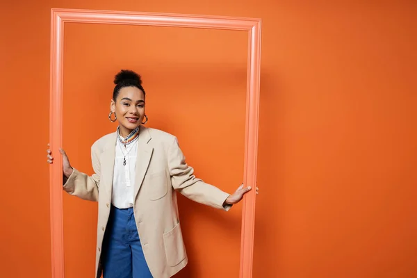 Щаслива афроамериканська модель моди в модному вбранні з аксесуарами, що тримають помаранчеву рамку — стокове фото