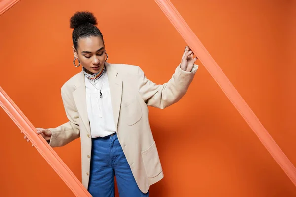 Stylish fashionista in beige blazer with hoop earrings and necklace holding orange framework — Stock Photo