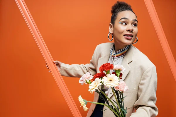 Schicke stylische Fashionista im trendigen Straßenoutfit mit orangefarbenem Rahmen und Blumenstrauß — Stockfoto