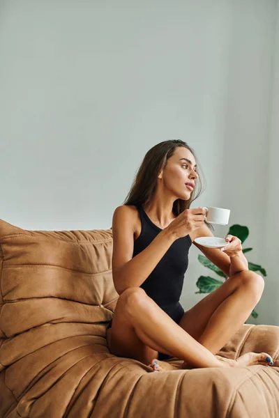 Bonita mujer joven con el pelo morena disfrutando de la taza de café, sentado en la silla cómoda bolsa de frijol - foto de stock