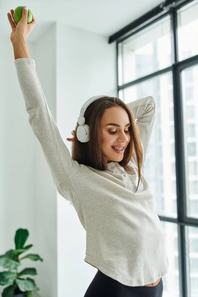Щаслива жінка з брекетами позує в довгому рукаві і трусиках, слухаючи музику в навушниках — стокове фото